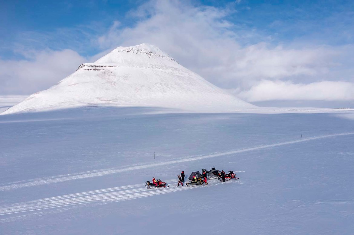 bilde av snødekt område med fjell i bakgrunnen og snøskutere på tur